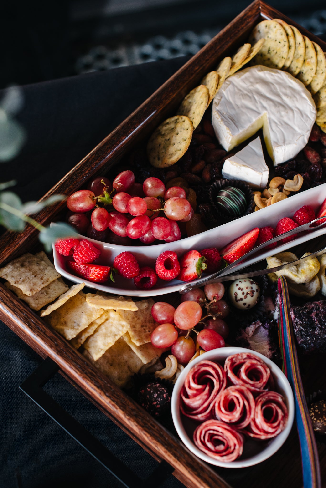 Charcuterie board with tomatoes and chives surrounding the bottle