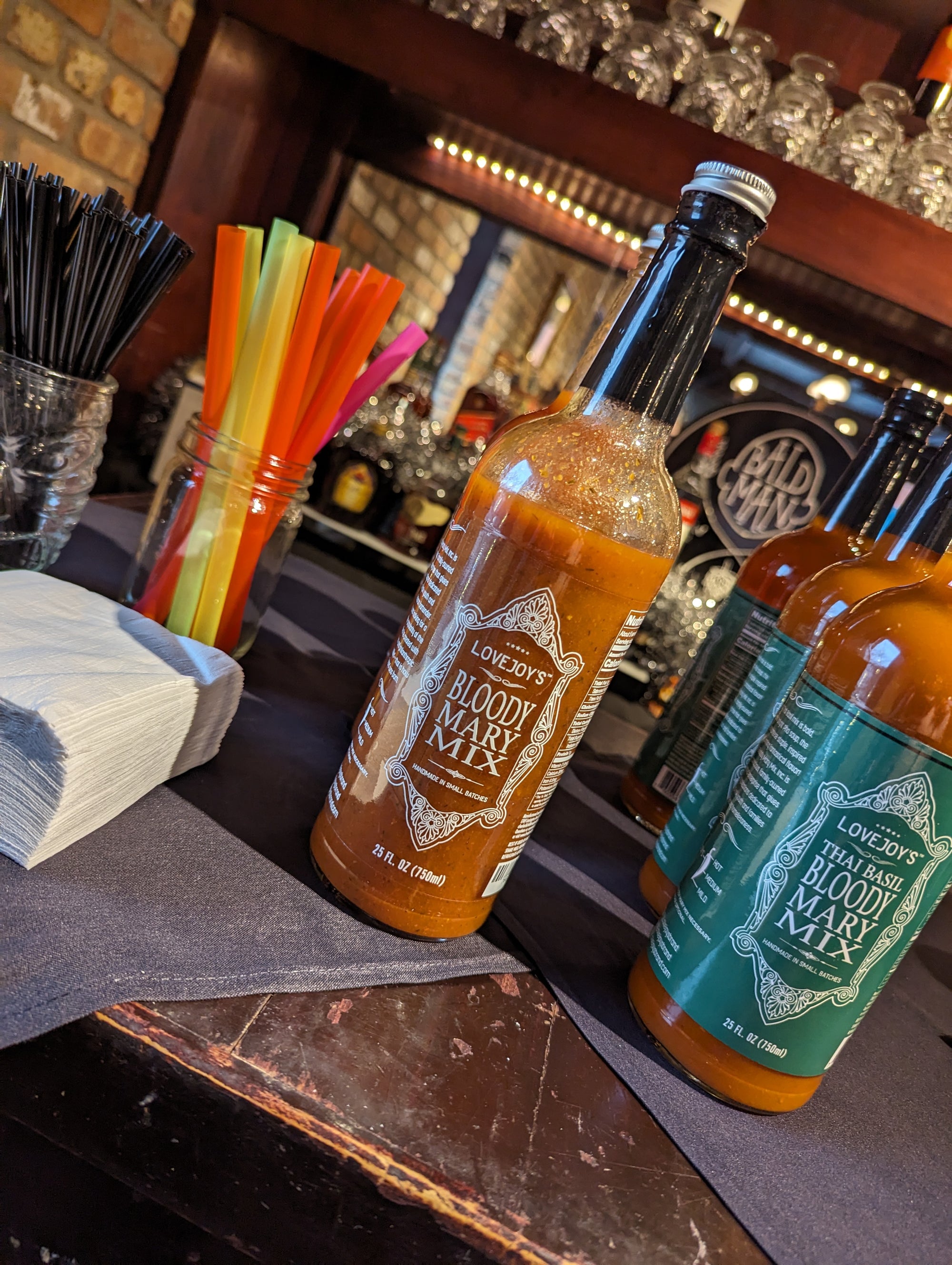 Two bottles sitting on a bar counter top with straws in a cup