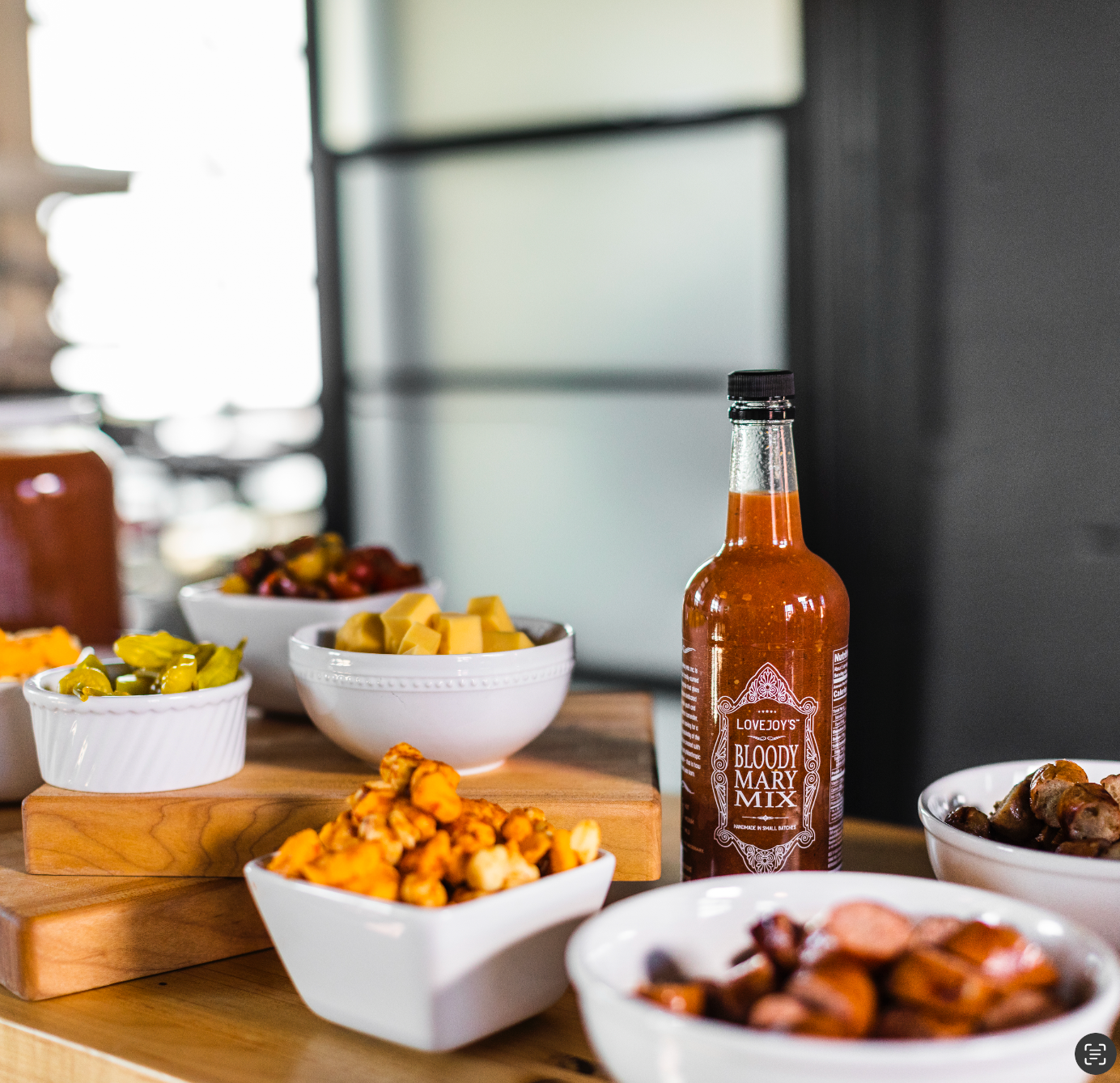 Table with bowls full of cheese, meat and a bottle of bloody mary mix