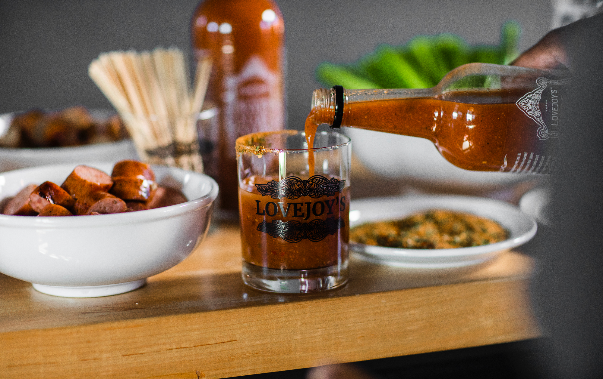 Pouring a glass bottle filled with bloody mary mix into a cup