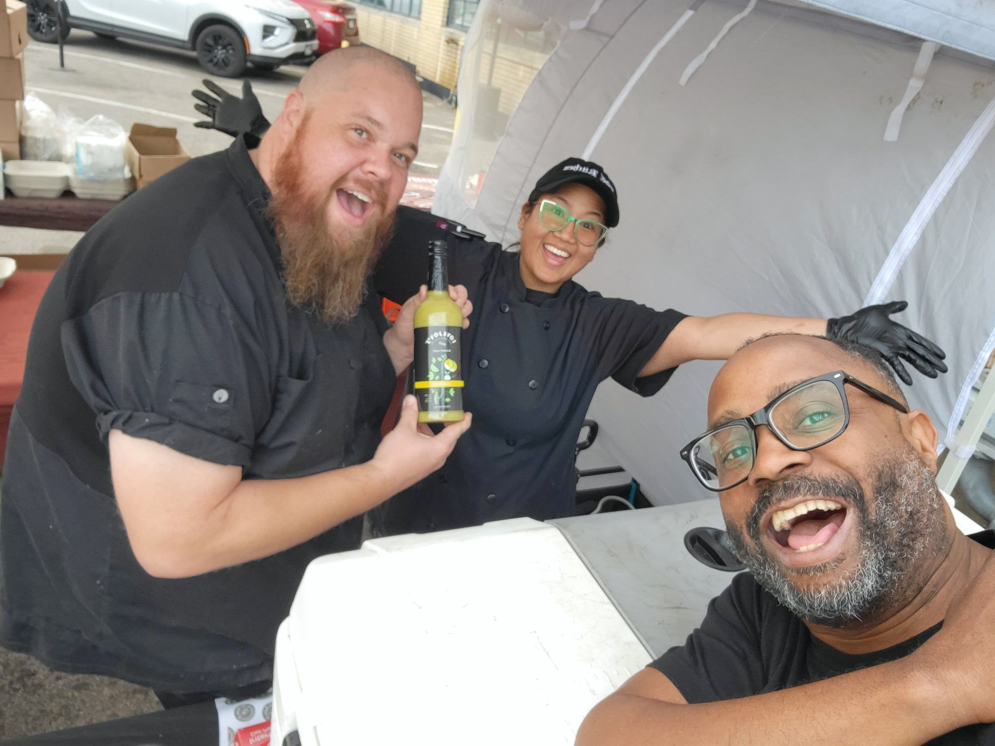 Lovejoy's employees holding up bottle of Bottle of Lovejoy's Chimichurri Bloody Mary Mix at market.