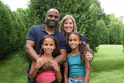 Family of four standing in a park with trees and grass