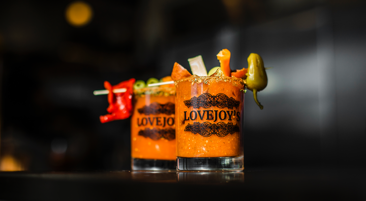 Two pickle-infused bloody mary mixes garnished with various ingredients, served in glasses.